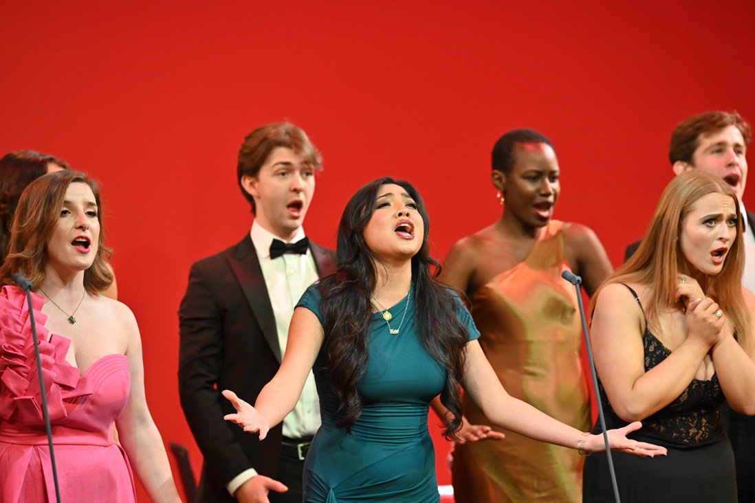 A group of students, wearing smart attire, singing on stage.